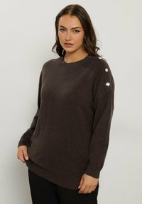 Maglione in maglia marrone con scollatura a girocollo, spalle cadenti e dettagli in bottone argentato sulla spalla sinistra. Texture morbida e vestibilità rilassata.