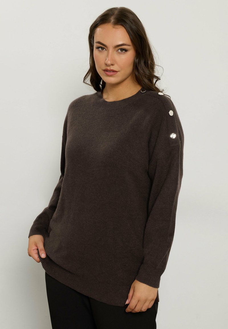 Maglione in maglia marrone con scollatura a girocollo, spalle cadenti e dettagli in bottone argentato sulla spalla sinistra. Texture morbida e vestibilità rilassata.