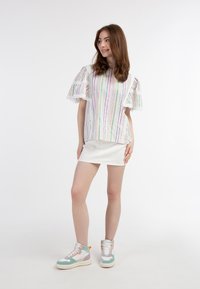Hvid, stribet bluse med flagrende blondeærmer parret med en hvid mini-nederdel og multifarvede højhælede sneakers med pastelaccenter.