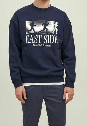 Homme portant un sweat-shirt bleu marine avec des figures blanches en train de courir et le texte "EAST SIDE New York Runners" sur le devant.