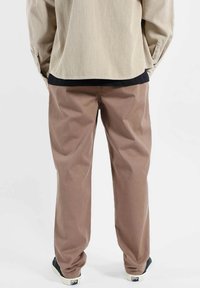 Chemise en velours côtelé beige à manches longues, associée à un pantalon marron clair. Le pantalon est ample et porté avec des baskets noires.
