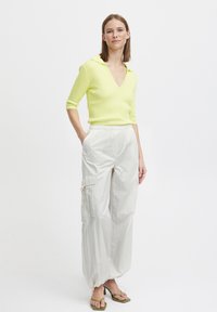 Lys grøn ribbet sweater med V-hals og korte ærmer, parret med løstsiddende, lysfarvede cargo bukser og grønne hælede sandaler.