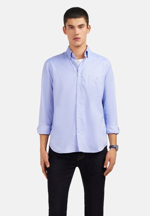Chemise légère bleu clair à manches longues, avec une poche poitrine et une coupe décontractée, assortie à un jean sombre. Tissu en coton doux, détails minimalistes.