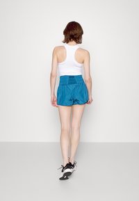 Blå sportshorts med smockat midjeband och en ljus vit linne, sedd bakifrån, tillsammans med svarta träningsskor.