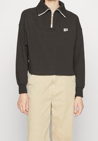 Pullover nero cropped con un motivo texturizzato, colletto e zip a quarto. Presenta un piccolo logo sul lato sinistro del petto e polsini a costine.