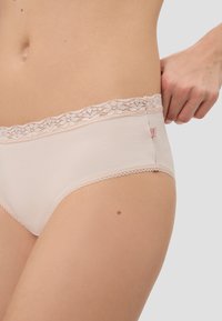 Beige Slips mit Spitzenbesatz und einer glatten, gerippten Textur. Verfügt über einen zarten Spitzenbund mit floralem Muster und einem kleinen Logостicker.