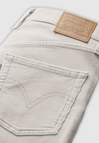 Calças de cotim brancas com uma superfície texturizada, apresentando um rótulo de couro castanho na cintura e um design de bolso traseiro costurado.