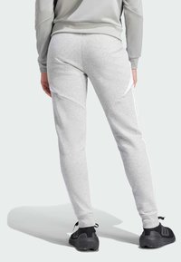 Grijze joggingsbroek van zacht materiaal, met witte zijstrepen, taps toelopende pijpen en een hoge tailleband. Zwarte sportschoenen maken de outfit af.