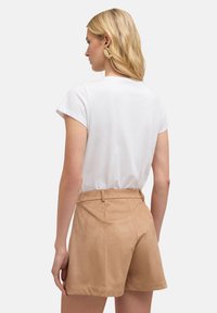 Pantalones cortos de ante sintético en tono beige con cintura alta y presillas para cinturón, combinados con una camiseta blanca de manga corta. Textura suave y ajuste entallado.