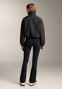 Giacca nera trapuntata con colletto alto, abbinata a leggings neri a palazzo. L'outfit presenta una finitura testurizzata ed è completato da sneaker bianche.