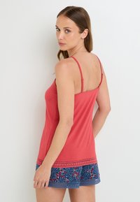 Haut sans manches rouge avec des bretelles réglables, présentant un ourlet décoratif. Assorti avec un short marine arborant un motif floral rouge et vert.