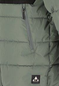 Puffjakke i olivengrøn med en sort øverste del. Har en grå lynlås lomme og et sort mærkepatch på højre side. Glat overflade.