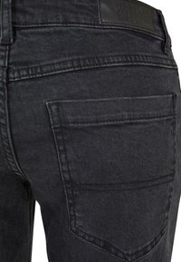 Jeans en denim noir avec une texture lisse, comportant deux poches arrière et des détails de couture subtils. Patch en cuir à la taille.