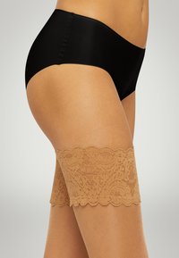 Collant alti beige in pizzo con un motivo floreale e bordo superiore a scallop, abbinati a un perizoma nero senza cuciture. Texture liscia.