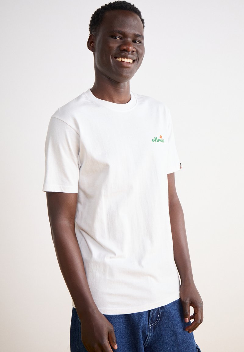 Camiseta de algodón blanca con un pequeño logo verde y rojo en el lado izquierdo del pecho. Cuello redondo clásico y manga corta. Diseño sencillo, ajuste relajado.