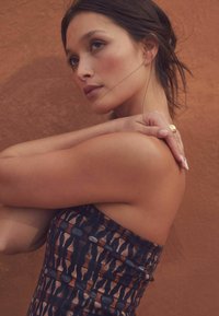 Strapless jurk met een veelkleurig patroon in donkere blauwtinten, bruin en beige. Glad stof met een getailleerd ontwerp. Huidskleur is warm.