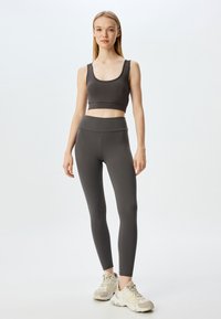 Harmaa urheiluliivi ja korkea vyötärö leggings, jotka on valmistettu sileästä ja joustavasta kankaasta. Ominaisuuksiin kuuluu lyhyt malli, leveät hihnat ja saumatön vyötärönauha.