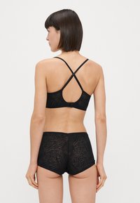 Conjunto de lingerie preto com um sutiã estampado com alças cruzadas e calcinhas de cintura alta combinando, ambos feitos de tecido texturizado.