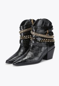 Bottines noires en matériau synthétique texturé. Présentent un bout pointu, un talon bloc, des sangles cloutées et tressées, avec des accents dorés.