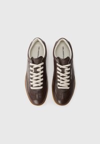 Sneaker in pelle marrone con finitura testurizzata, lacci crema e suola in gomma a contrasto. Presenta una punta rotonda e un branding sottile.