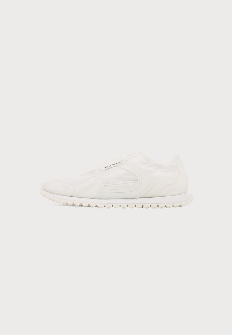 Sneaker blanche sans lacets avec semelle texturée, tige élastique et design cousu subtil, montrée de profil sur un fond uni.