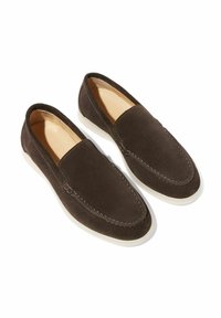 Brune ruskindssko uden snørebånd med hvide gummisåler, der har stikninger og en glat, afrundet form.