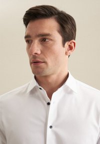 Witte katoenen shirt met een button-down kraag, voorzien van marineblauwe knopen en een patroontje aan de binnenzijde van de kraag. Gladde textuur en slim fit.