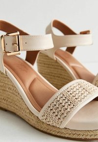 Sandales compensées beiges avec une bride ajustable à la cheville, dotées d'un dessus en tissu tissé, d'accents en cuir lisse et d'une semelle enveloppée de jute.