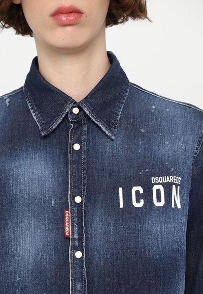 Tumedast sinine teksajakk kergete kulumistega. Omab klassikalist kraed, esipoolseid nuppe ja valget "ICON" logo. Punane brändi silt on nähtav.