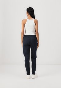 Marinblå joggingbyxor med elastisk midjeband, sidofickor och mudd runt anklarna, kombinerade med en vit linne. Mjuk tygstruktur.