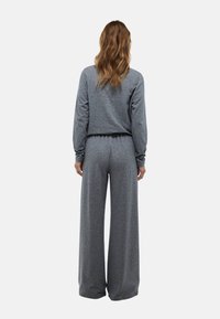 Haut gris à manches longues, coupé et avec une taille élastique, associé à un pantalon à jambes larges. Texture douce et coupe décontractée.