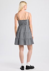 Black and white gingham dress with a smocked bodice, tiered skirt, and thin adjustable straps. Worn with black shoes and white socks.