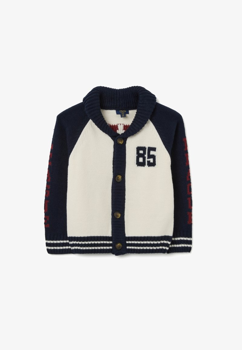 Cárdigan de punto en azul marino y crema con cuello de chal, cinco botones marrones, impresión "85" en el pecho y texto rojo en las mangas con ribete a rayas.