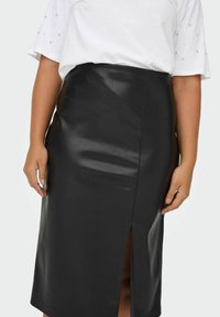 Melnā mākslīgā āda midi svārki ar priekšējo šķēlumu, gluda tekstūra un pieguļošs siluets. Apvienots ar balto T-kreklu ar dekoratīviem elementiem.