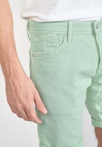 Shorts en denim vert menthe avec des revers, design à cinq poches et couture contrastante. Tissu en coton texturé. Poche pour stylo sur le côté.