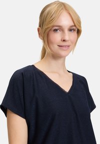 Marineblaues Kurzarmoberteil mit einem V-Ausschnitt, aus einem strukturierten, schimmernden Stoff gefertigt, mit einem entspannten Schnitt und minimalen Nähten.