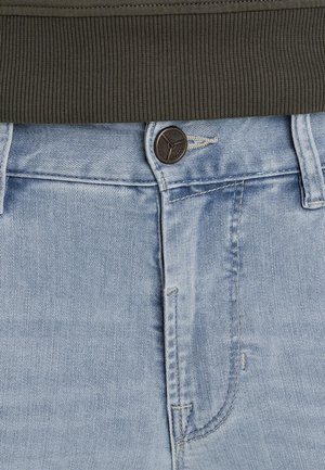 Světle modré džíny z denimu s klasickým designem, které mají hnědé zapínání na knoflík a tmavě zelený žebrovaný pás.