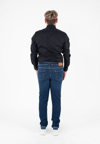 Camicia nera a maniche lunghe, jeans in denim blu con un'etichetta in pelle sul retro e sneakers bianche. Texture liscia e design aderente.