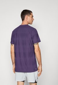 Lilla atletisk t-shirt med en struktureret design med lodrette linjer, korte ærmer og rund halsudskæring, parret med lysegrå shorts.