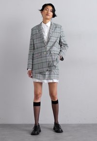 Pilkas languotas bleizeris su dideliais apykaklėmis ir mygtuko uždarymu, derinamas su baltu marškinėliu ir sijonu. Juodi iki kelių siekiantys kojinaitės ir sijoninės bateliai.