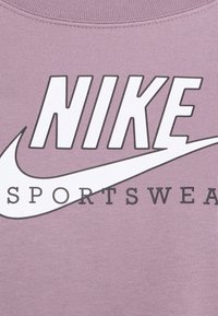 Lila sweatshirt med en stor vit Nike-logotyp med grå kontur och ordet "SPORTSWEAR" i svart under. Slät yta.