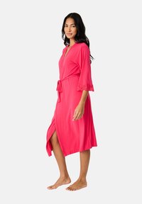 Accappatoio rosa con maniche a tre quarti, bordo in pizzo sulle maniche, design avvolgente, lunghezza a metà polpaccio e spacco laterale. Tessuto morbido e vestibilità comoda.