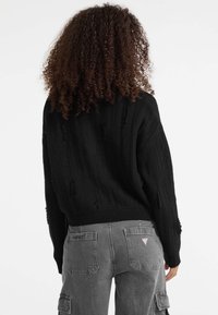 Maglione nero a coste con dettagli strappati, maniche ampie e un taglio corto, abbinato a pantaloni cargo grigi con tasche a toppa.