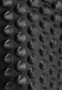 Texturierte schwarze Oberfläche mit erhabenen runden Nieten, die in einem Rastermuster angeordnet sind und ein taktiles sowie visuell auffälliges Design schaffen.