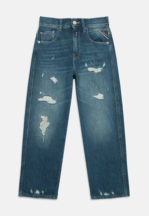 Jean en denim bleu avec des patches usés, design cinq poches et fermeture par bouton métallique, posé à plat sur un fond blanc.