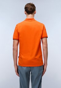 Oranžové polo tričko s krátkým rukávem, kontrastním černým lemem límce a minimalistickým designem. Tkanina působí hladce a lehce.