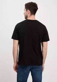 Czarna bawełniana koszulka z klasycznym okrągłym dekoltem, krótkimi rękawami i prostym krojem, noszona z jasnoniebieskimi dżinsami.