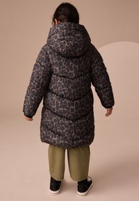 Pikowana kurtka w cętki geparda, z kapturem, ściągaczami na rękawach i sięgająca do kolan. Noszona na zielonych spodniach i czarnych butach.