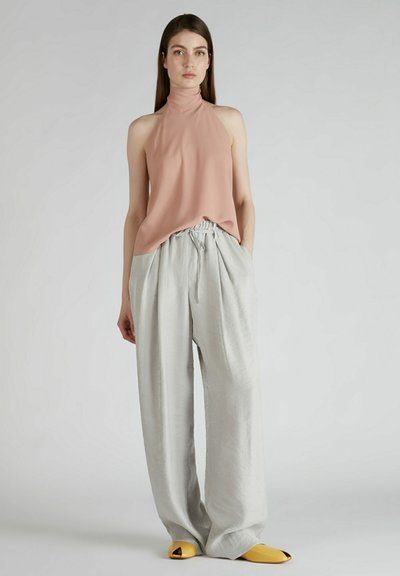 Top na halter w miękkim różowym materiale zestawiony z jasnoszarymi spodniami o szerokich nogawkach. Żółte sandały na otwartym palcu dopełniają outfit.