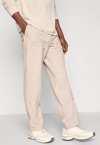 Heledad beežid püksid laia lõikega, küljetaskudega; kombineeritud valgete ja beežide spordijalatsitega. Pehme kangastekstuuri.